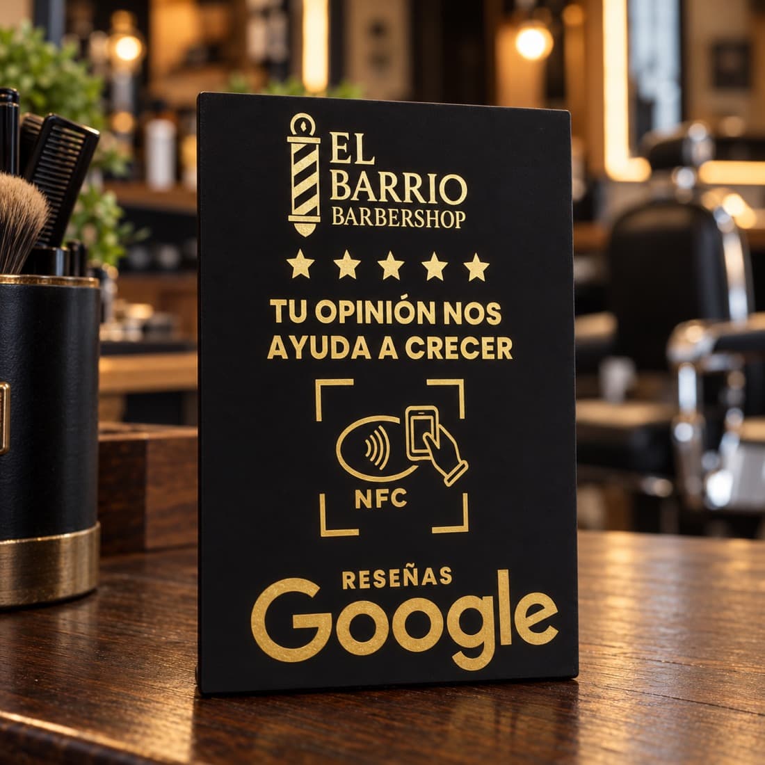 Placa negra con letras doradas de El Barrio Barbershop que invita a dejar una reseña en Google con NFC, sobre el mostrador de la barbería